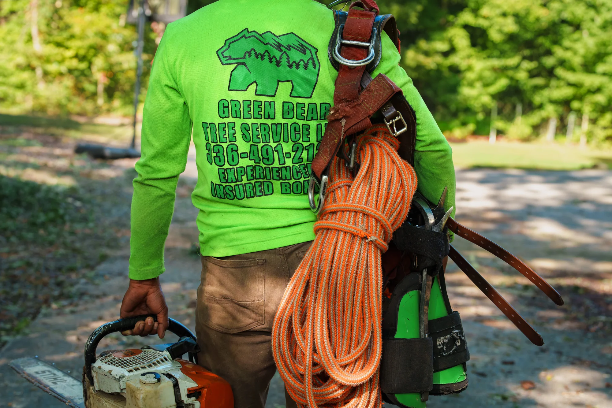 Green Bear worker carrying climbing gear and a chainsaw